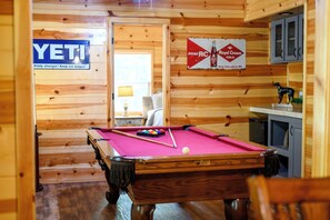 Una habitación de madera con una mesa de billar, un letrero de YETTI y un letrero de Royal Crown Cola.