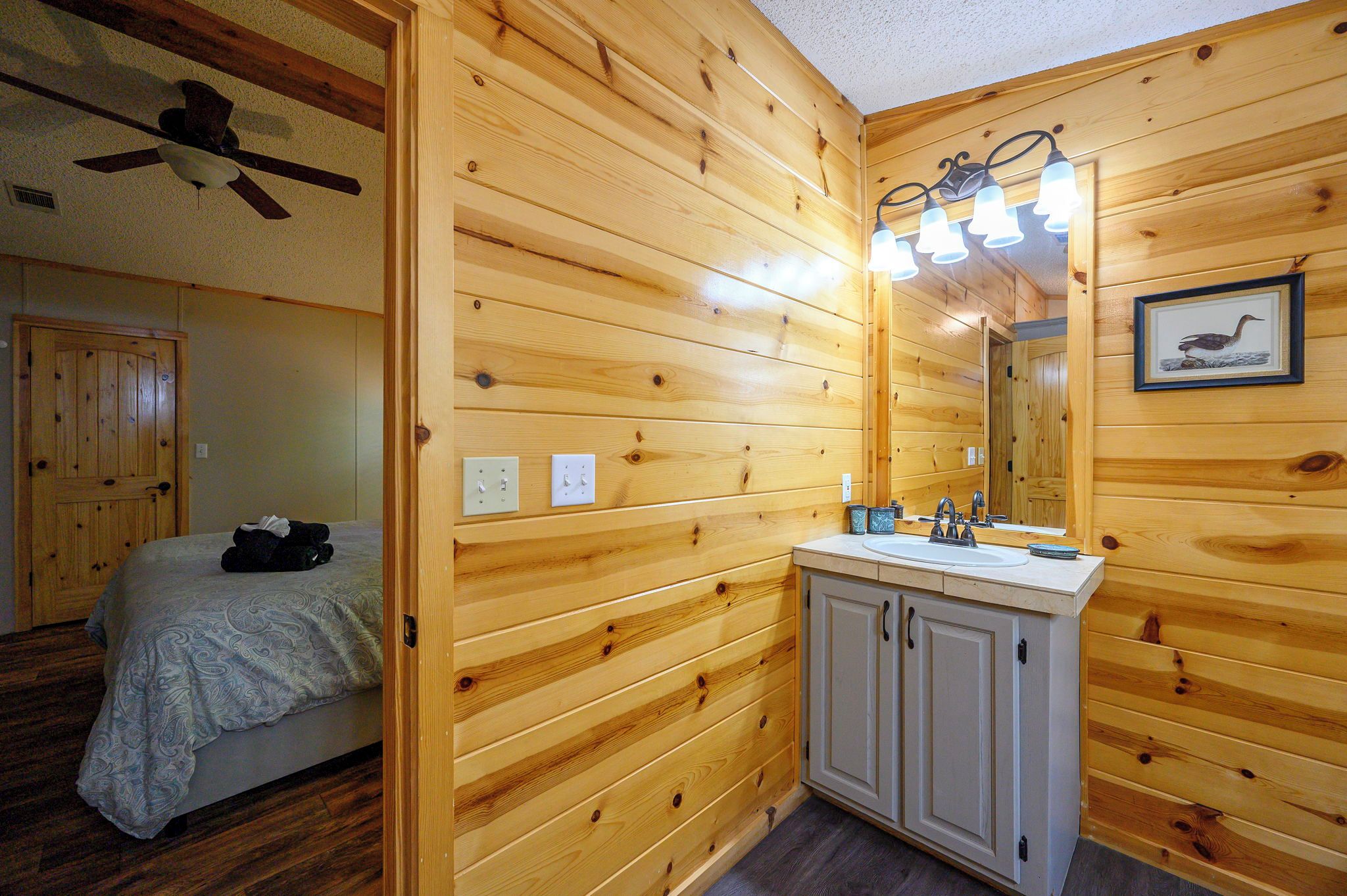 A wooden-paneled room with a bed, a bathroom with a sink and mirror, and a ceiling fan.