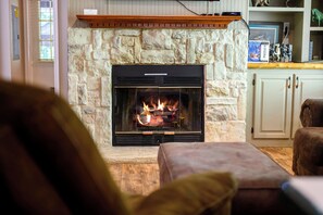 Una chimenea de piedra con fuego, una repisa de madera y un televisor encima.