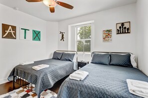 Ein Schlafzimmer mit zwei Betten, einem Deckenventilator und Wandbildern, darunter Buchstaben und eine Silhouette.