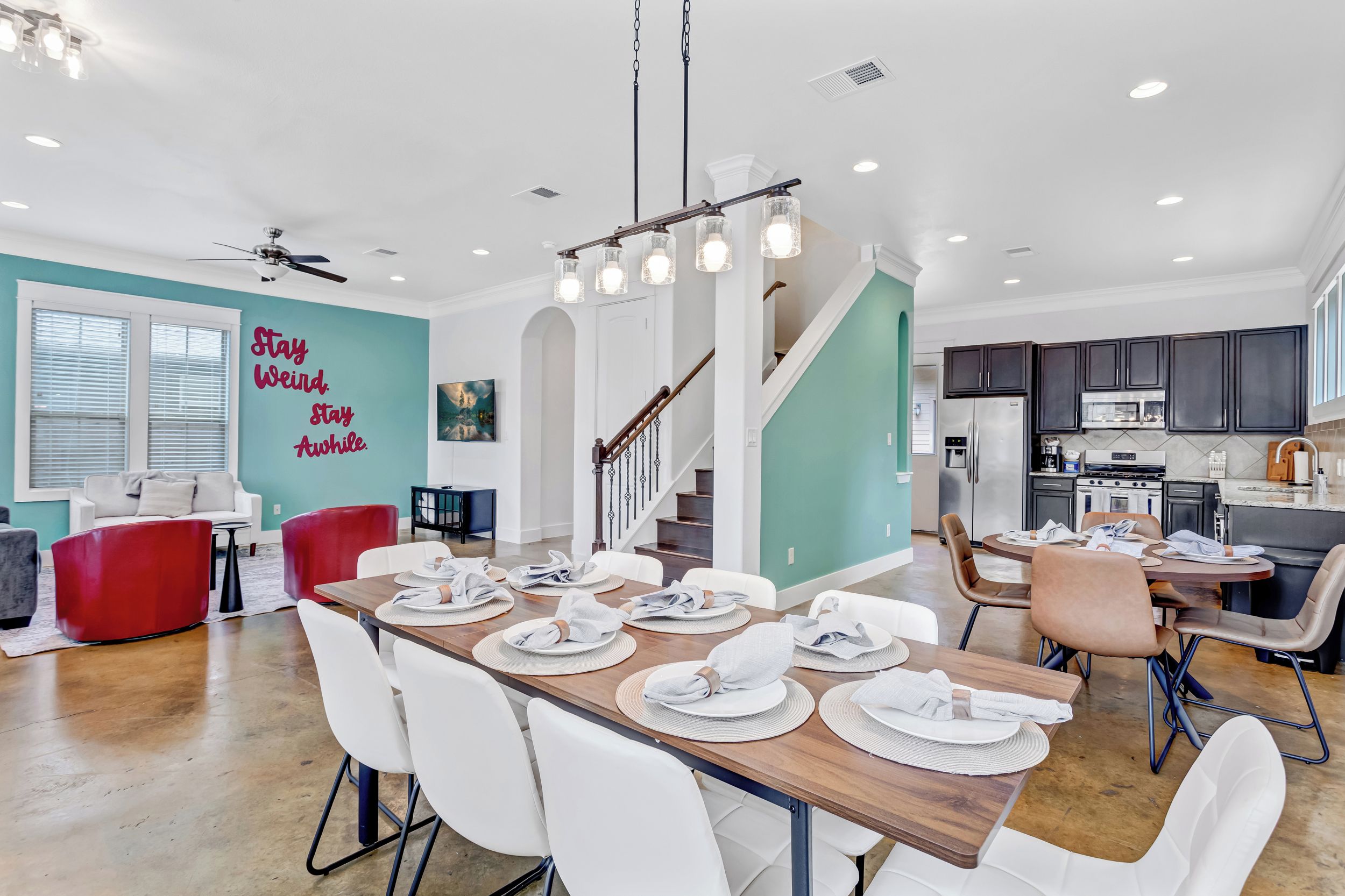 A spacious dining area with a long table set for multiple people, a kitchen with modern appliances, and a staircase leading to another level.