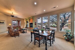 A spacious living room with a fireplace, a dining area with a wooden table and chairs, and large windows offering a view of a desert landscape.