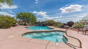 A pool area with two hot tubs, surrounded by trees and rocks, under a clear sky.