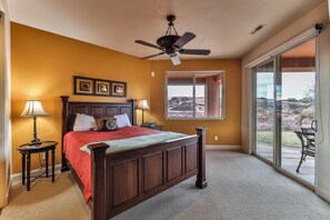 Ein Schlafzimmer mit einem Bett, zwei Nachttischen, einem Deckenventilator, einem Fenster mit Blick ins Freie und einer Glastür zum Patio.