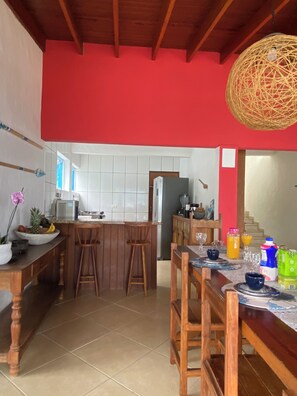 Eine Küche mit roter Wand, Holzbarhocker, einem Esstisch mit Stühlen und einer Pendelleuchte.