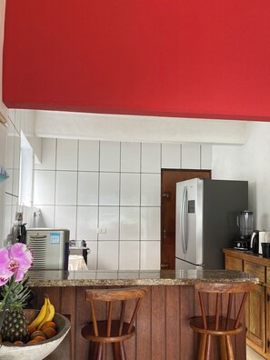 Eine Küche mit weißen Fliesen, einem Kühlschrank, einem Mixer und Holzbarhocker.