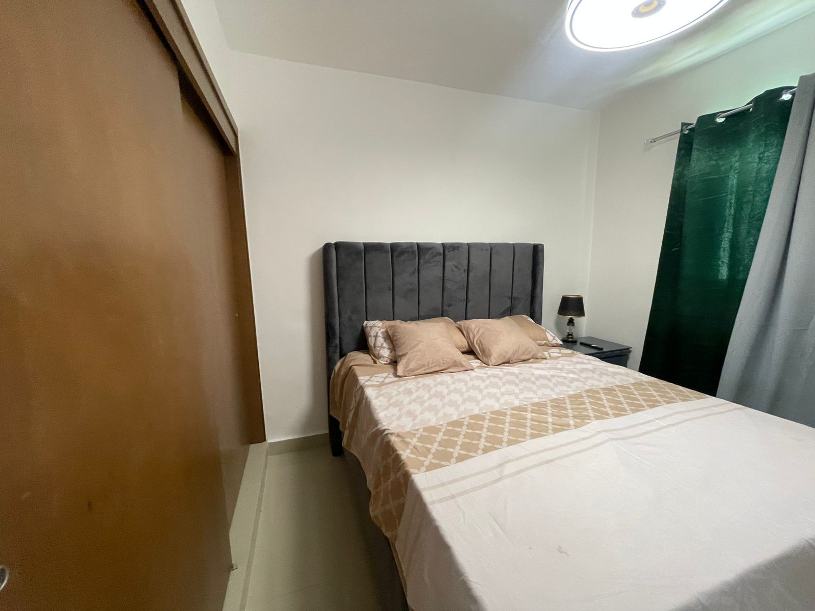 Une chambre à coucher avec un lit, une table de chevet, une lampe et un rideau vert.