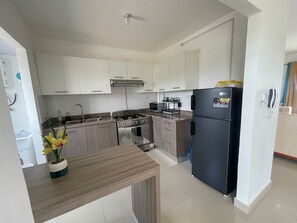 A modern kitchen with white cabinets, a black refrigerator, a stove, and a microwave. - APARTAMENTO COMPLETO A 2 MINUTOS DE LA PLAYA CON PISCINA 3 DORMITORIOS 2 BAÑOS (La Romana)