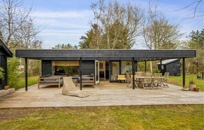 Un'area relax esterna moderna con terrazza in legno, posti a sedere e patio coperto.