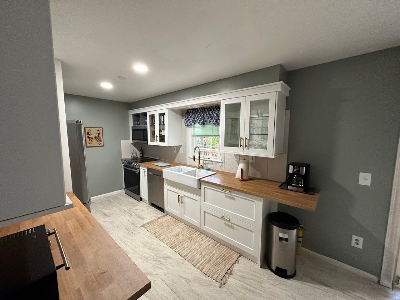 Una cocina moderna con armarios blancos, encimera de madera y pileta de acero inoxidable.