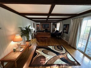 A spacious living room with a wooden floor, a large abstract rug, a sofa, a coffee table, a lamp, and a potted plant. - Gorgeous 4-bedroom house with AC in charming Potomac (Potomac)