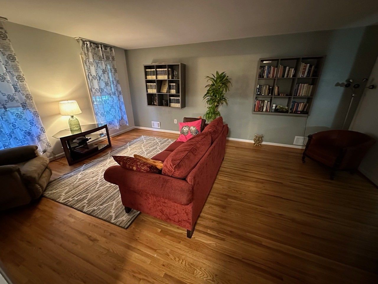 Uma sala de estar com um sofá vermelho, uma mesa pequena com abajur, uma estante de livros e um vaso com planta.