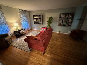 Ett vardagsrum med en röd soffa, ett litet bord med en lampa, en bokhylla och en krukväxt.