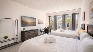 A hotel room with two beds, a desk, a chair, a TV, and a window with curtains. - Cozy Beach Studio | Sleeps 4 | First floor (Myrtle Beach)