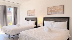 A hotel room with two beds, a window with curtains, and two wall-mounted paintings. - Cozy Beach Studio | Sleeps 4 | First floor (Myrtle Beach)
