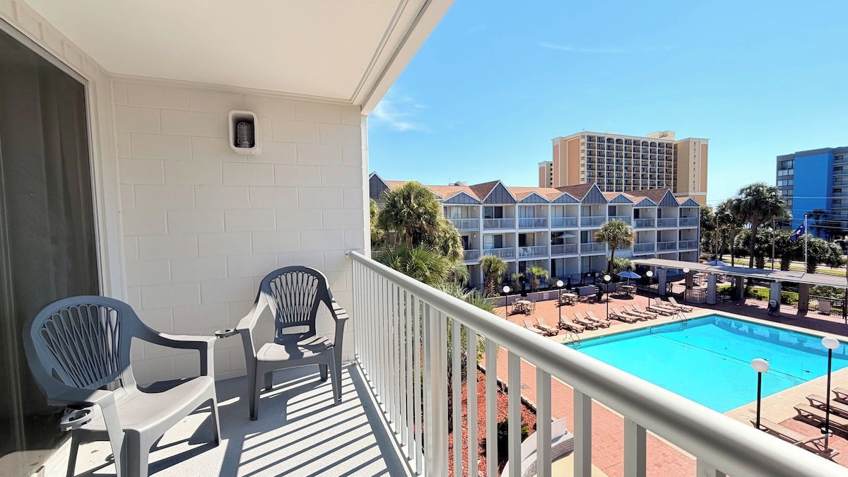 Ein Balkon mit zwei Stühlen, einem Pool und Blick auf einen Hotelkomplex.