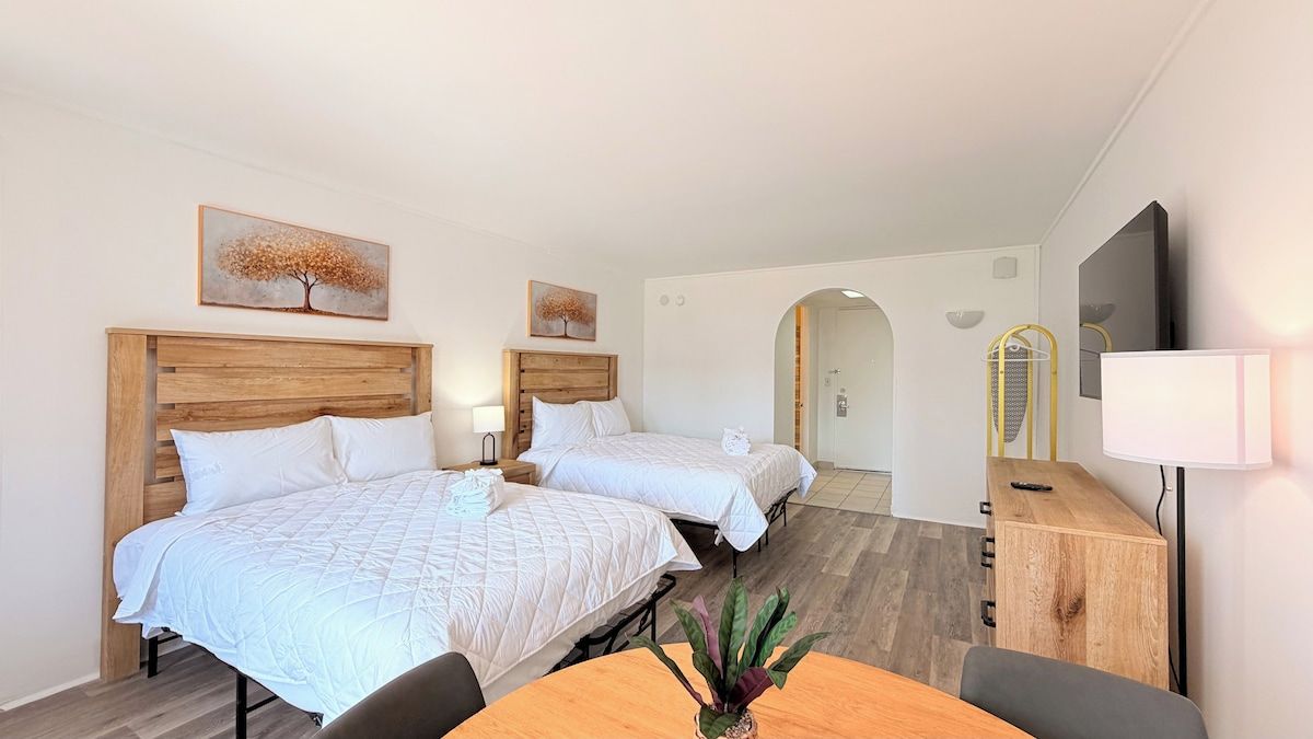 Een hotelkamer met twee bedden, een houten hoofdbord, een bureau, een stoel, een televisie en een spiegel.