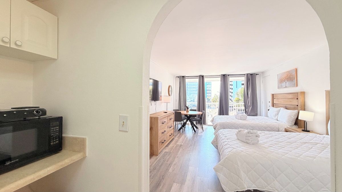 Quarto de hotel com cozinha compacta, duas camas, escrivaninha e vista para a cidade.