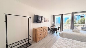 Quarto de hotel com cama, escrivaninha, televisão e varanda com vista para edifícios.