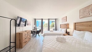 Ein Hotelzimmer mit zwei Betten, einem Schreibtisch, Stühlen, einem Fernseher und einem Balkon mit Blick.