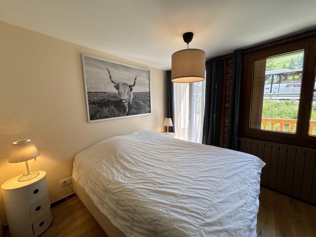 A bedroom with a bed, a lamp, a window with curtains, and a picture on the wall.