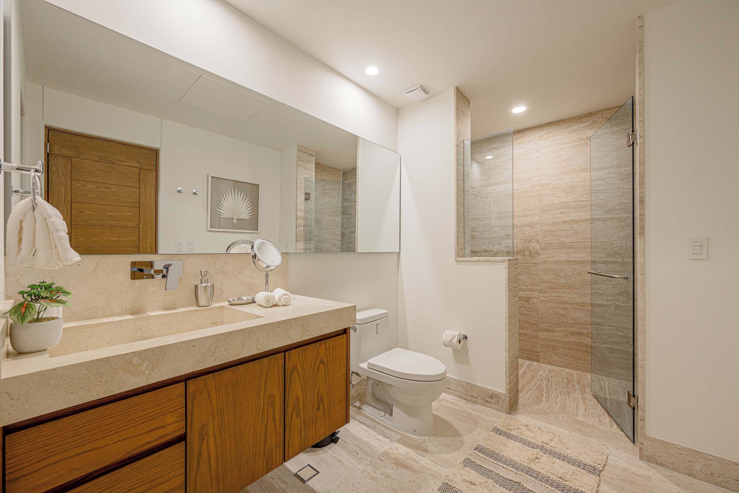 A modern bathroom with a large mirror, a sink with a wooden cabinet, a toilet, and a glass shower enclosure.