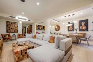 A modern living room with a sectional sofa, a coffee table, and a dining area with a wooden table and chairs. - Beachfront 3BR Condo at Tortuga Bay by The Agency Baja Travel (San José del Cabo)