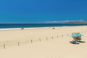 A beach with a lifeguard station, a fenced area, and a distant mountain. - Beachfront 3BR Condo at Tortuga Bay by The Agency Baja Travel (San José del Cabo)