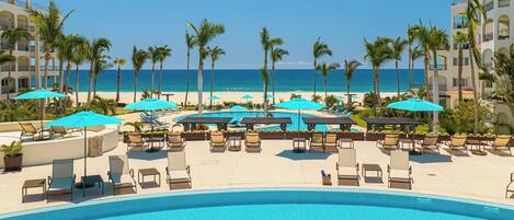 A resort pool area with lounge chairs, umbrellas, and a view of the ocean.