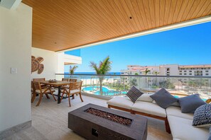 Un balcon doté d’un plafond en bois, une table à manger avec des chaises, un canapé avec des coussins et un foyer.
