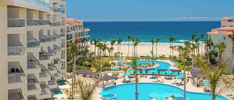 A resort with a large pool area, palm trees, and a view of the ocean.