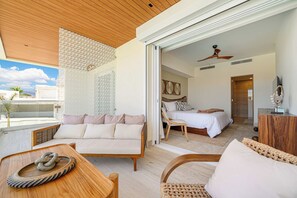 Une chambre d’hôtel moderne avec un balcon, un lit avec une literie blanche, une tête de lit en bois et un ventilateur de plafond.