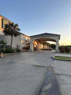 Entrada de hotel con camino cubierto, palmeras y cielo despejado.
