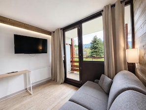 A modern living room with a flat-screen TV, a sofa, a small table, and a sliding glass door leading to an outdoor area. - 20m from ski slopes, 1st floor, balcony, tv, ski locker, 35m², Les Menuires (Les Menuires)