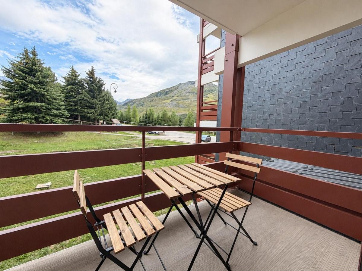 Un balcon avec une table et des chaises en bois, un mur en pierre et une vue sur les arbres et les montagnes.