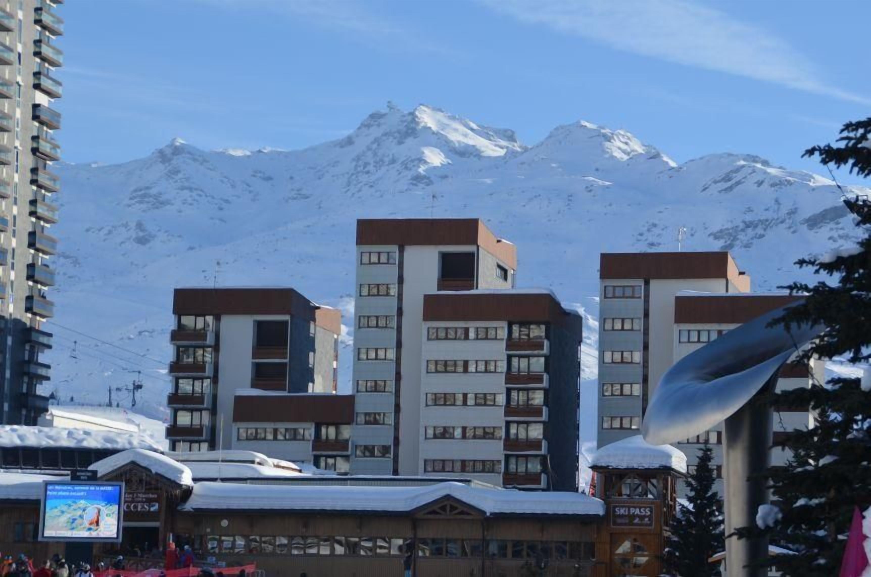 Ett hotell med flera våningar, en skylt som visar var man kan köpa liftkort och en snötäckt bergskedja i bakgrunden.