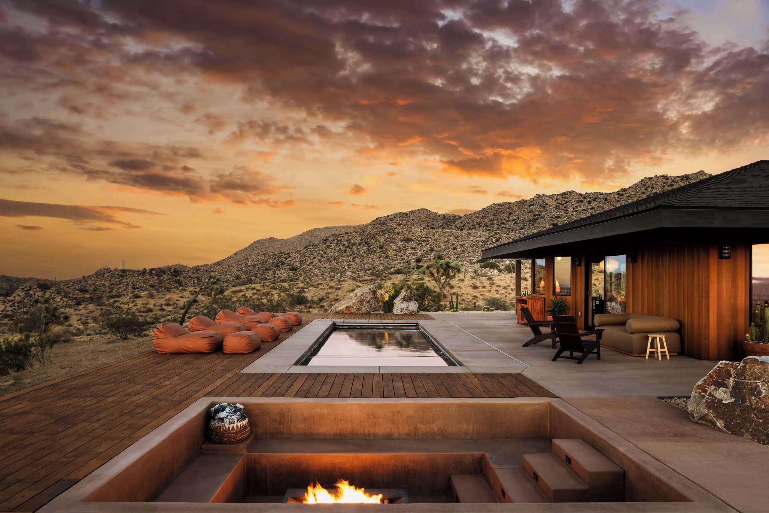 A desert landscape with a pool, outdoor seating, and a building with a wooden exterior.
