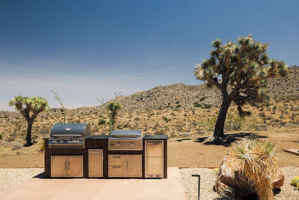 An outdoor grill setup in a desert landscape with cacti and a clear sky.