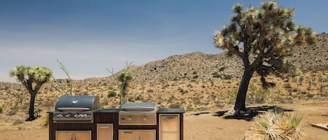 An outdoor grill setup in a desert landscape with cacti and a clear sky.