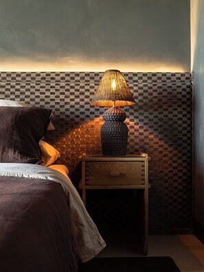 Ein Schlafzimmer mit karierter Wand, einem Nachttisch mit Lampe und einem Bett mit Kissen.