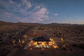 A desert landscape with a modern house featuring a swimming pool and outdoor lighting. - Solace House · Borders JT Park, Pool, Hot Tub (Joshua Tree)