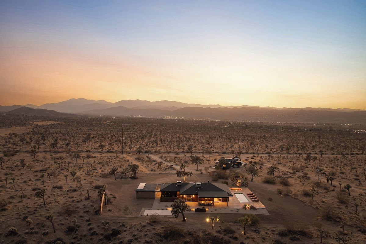 Un paysage désertique avec une maison moderne dotée d’un toit plat, de grandes fenêtres et d’un patio.