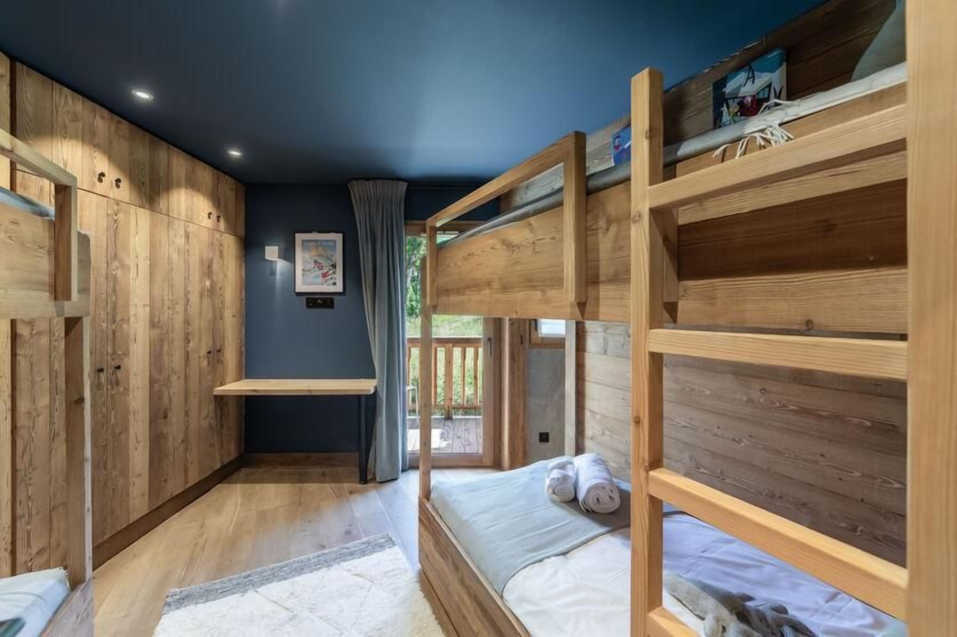 A room with bunk beds, wooden walls, and a window with curtains.