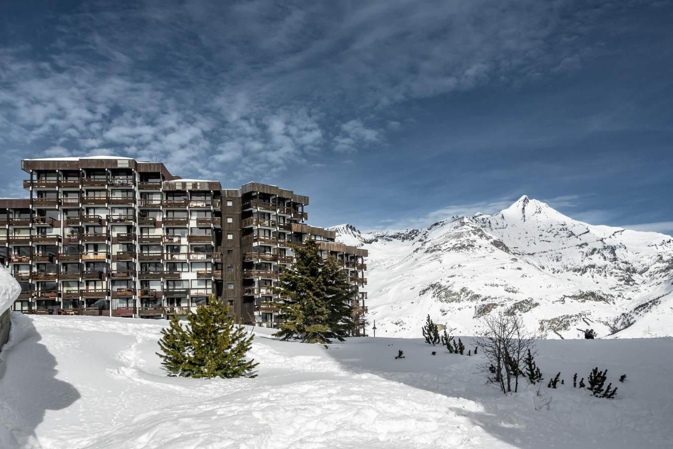 Un immeuble moderne à plusieurs étages, doté de balcons, qui se dresse sur fond de montagnes enneigées.