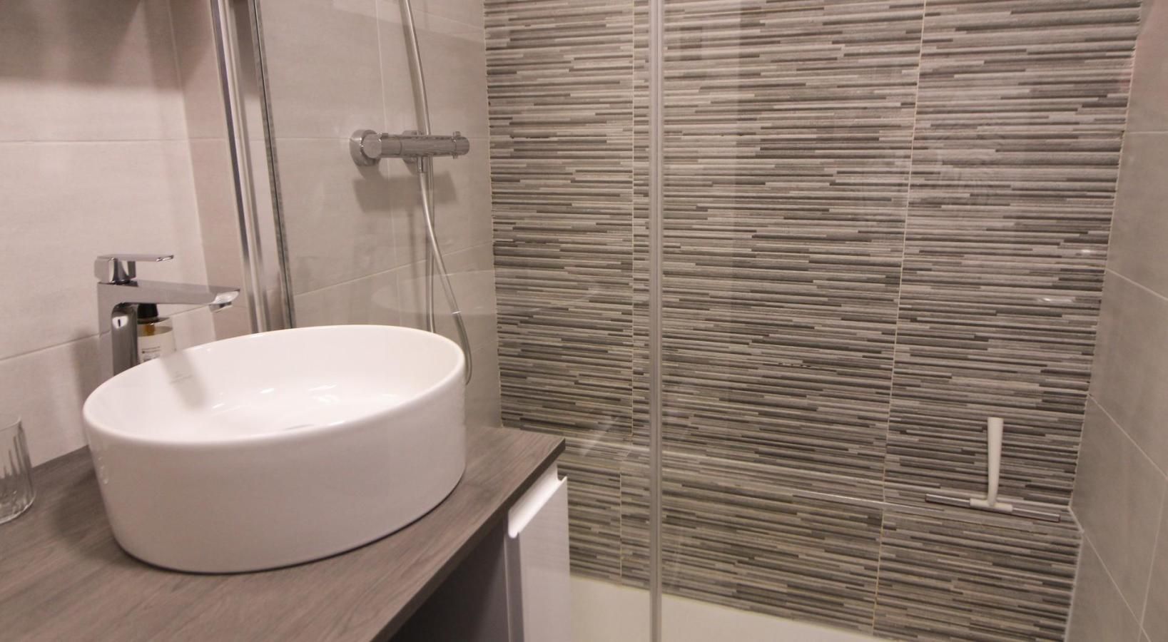 A modern bathroom with a round sink, a glass shower enclosure, and a textured wall.