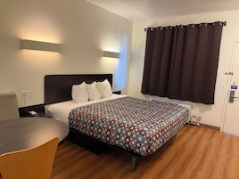 Habitación de hotel con cama, mesita de noche, silla y ventana con cortinas.