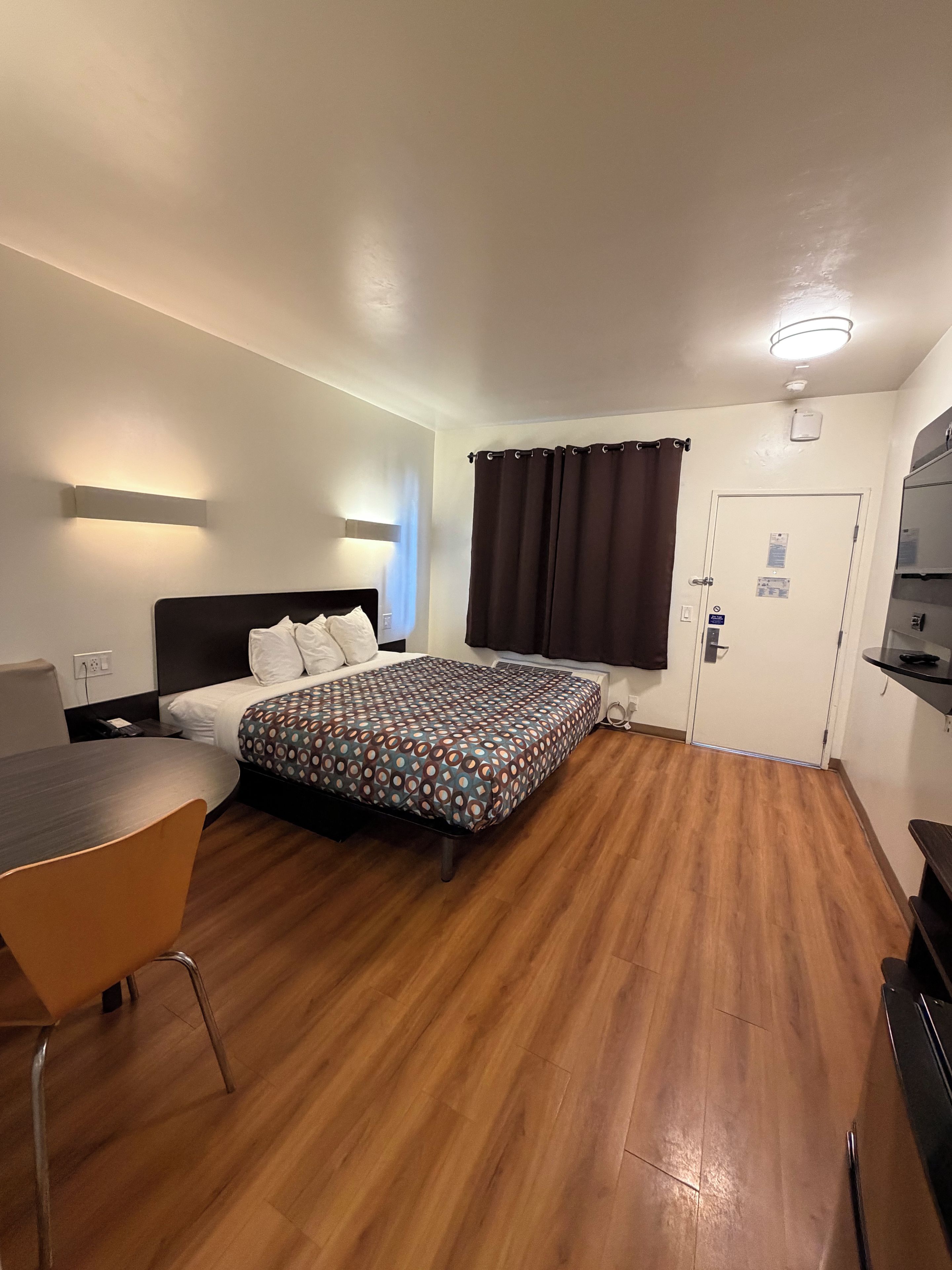 Habitació d'hotel amb llit, escriptori, cadira, porta i taula petita.