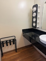 Un baño con encimera negra, lavabo blanco, toallero y espejo con repisa.