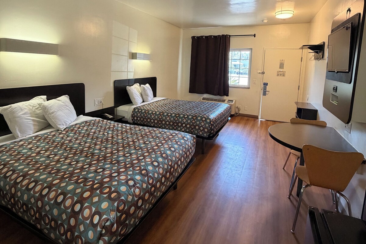 A hotel room with two beds, a desk, a chair, a television, and a window with curtains.