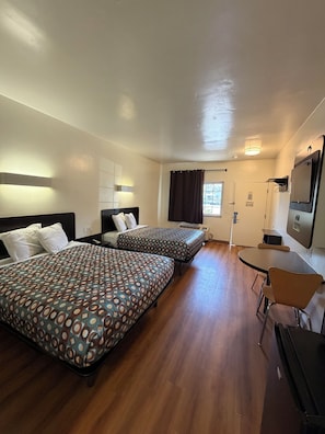 A hotel room with two beds, a desk, a chair, a television, and a window with curtains. - Odyssey Inn (National City)